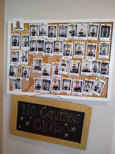 Corkboard covered in photos of kids labeled No Cavities Club