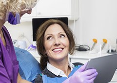 Older woman in dental chair smiling at dental assistant