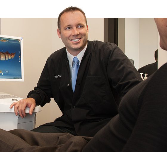 Doctor Vacek talking to dental patient in front of computer monitor showing digital scans of teeth