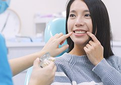 Woman in dental chair pointing to her smile