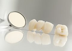 Dental crown and dental bridge resting on table next to dental mirror