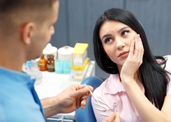 A female patient holding her cheek in pain as a dentist prepares to check her mouth for possible infection