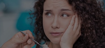 Woman with curly hair holding her cheek in pain