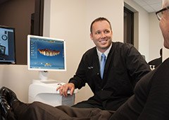 Doctor Vacek talking to a dental patient next to computer monitor showing digital scans of teeth