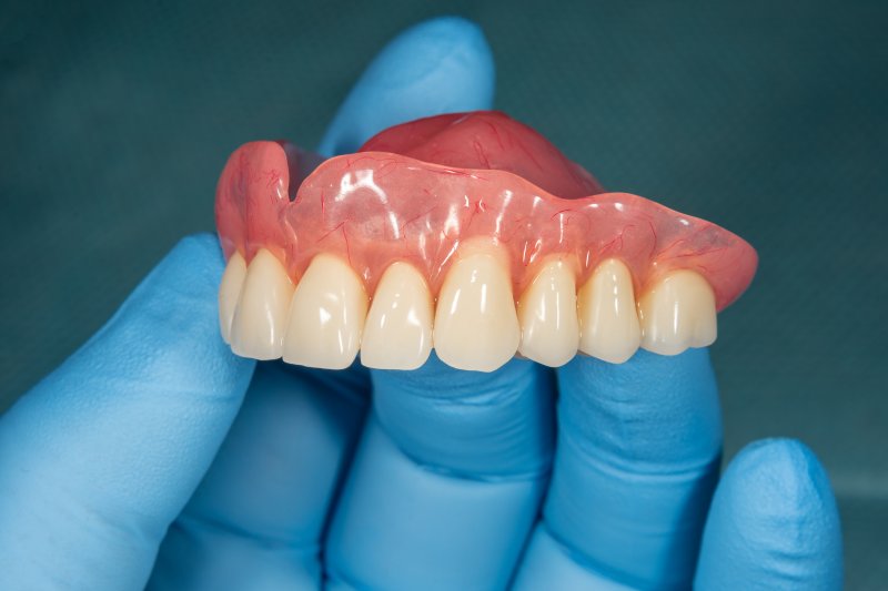 an up-close image of a gloved hand holding an upper denture